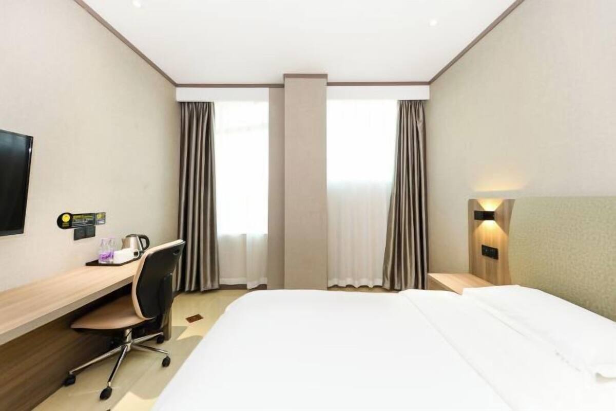 Una camera d'albergo con un letto, una scrivania, una sedia e un televisore appeso al muro.