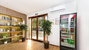 A hotel lobby with wooden flooring, a Coca-Cola refrigerator, a bookshelf, and two potted plants. - Jizhu Auto Business Hotel (Shanghai)