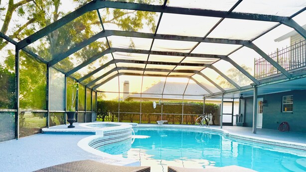 A covered swimming pool with lounge chairs, a hot tub, and a view of a house in the background. - Tampa Luxury 5BR Estate with Pool + Golf Views (Tampa)
