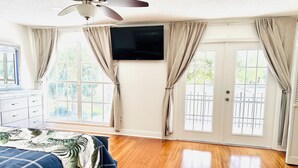 A bedroom with a bed, a ceiling fan, a TV, and large windows with curtains. - Tampa Luxury 5BR Estate with Pool + Golf Views (Tampa)