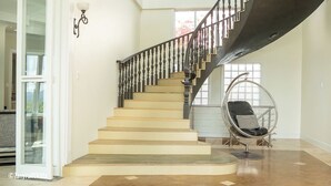 Un interior espacioso con una escalera curva, un sillón colgante y un ventanal grande.