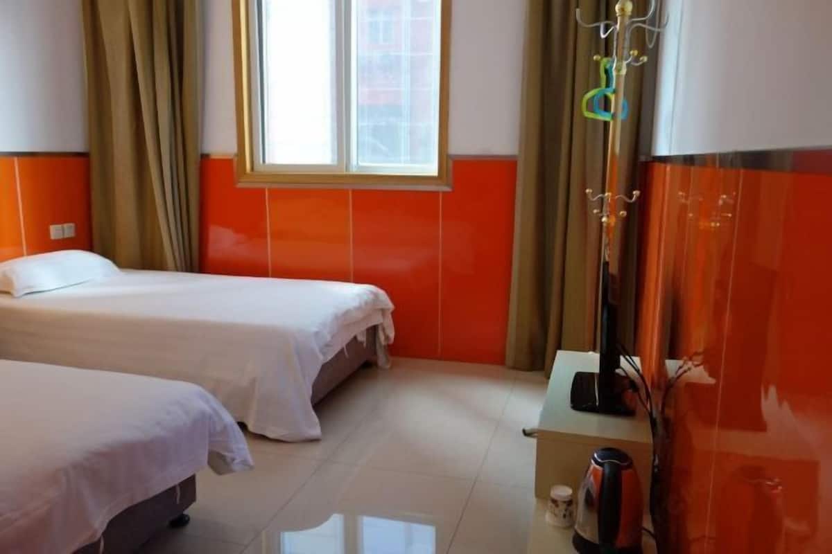 A hotel room with two beds, a window with curtains, a small table with a kettle, and a mirror.
