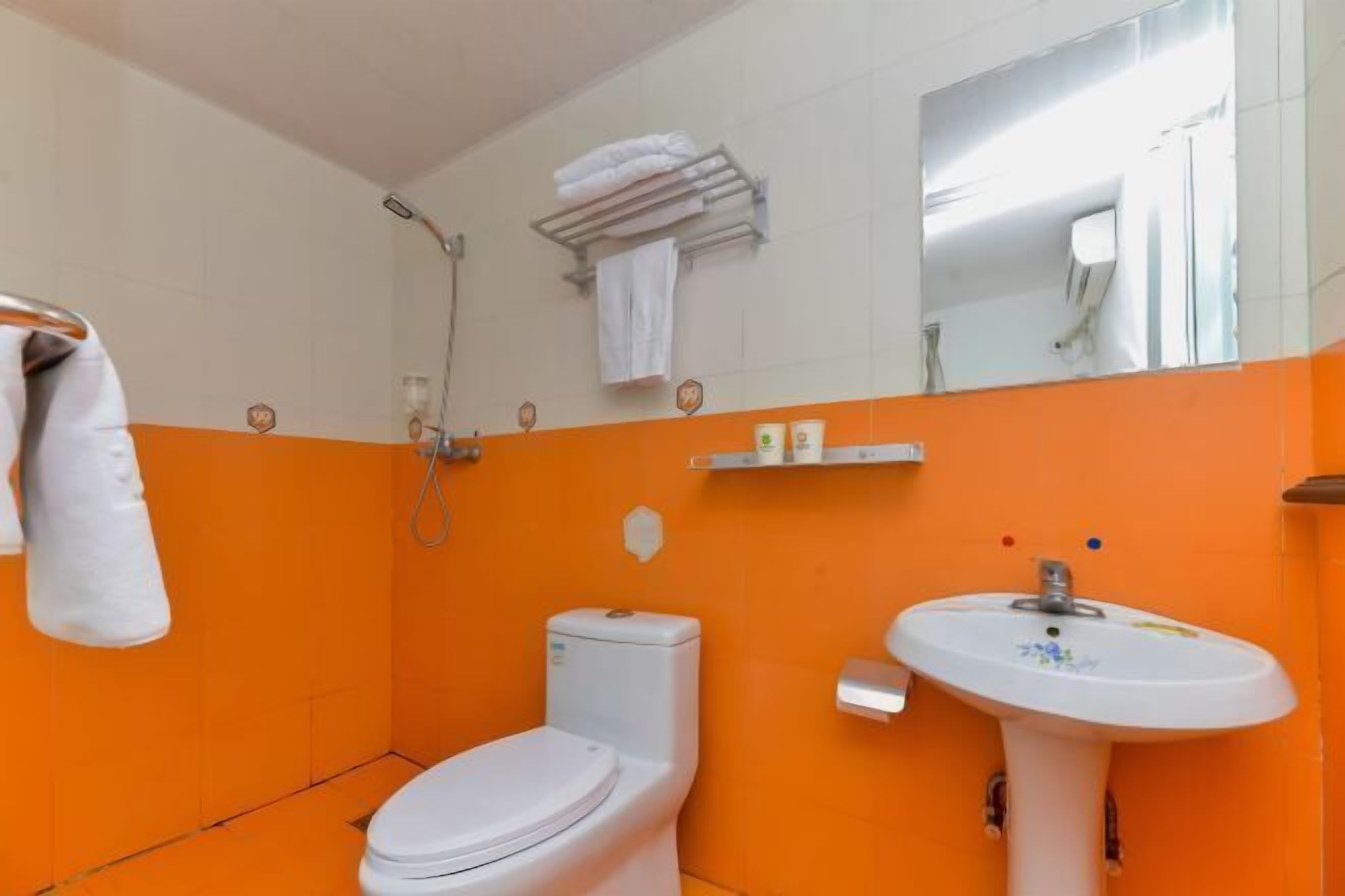 A bathroom with a white toilet, an orange wall, a white sink, and a towel rack with a towel.