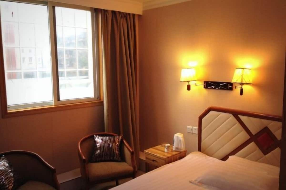 A hotel room with a bed, a chair, a nightstand, and a window with curtains.