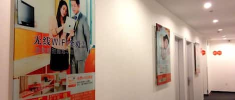 A corridor with posters on the wall, doors on the right, and a plain ceiling.