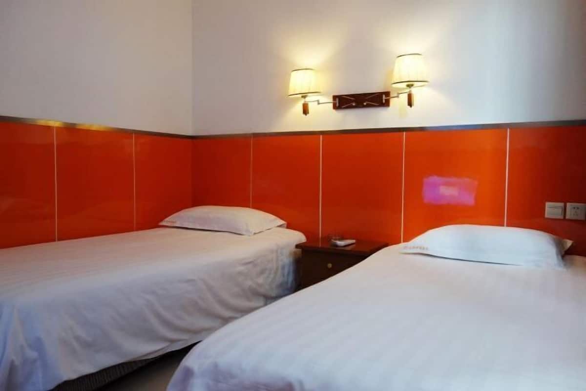 A hotel room with two single beds, a nightstand, and two wall-mounted lamps.