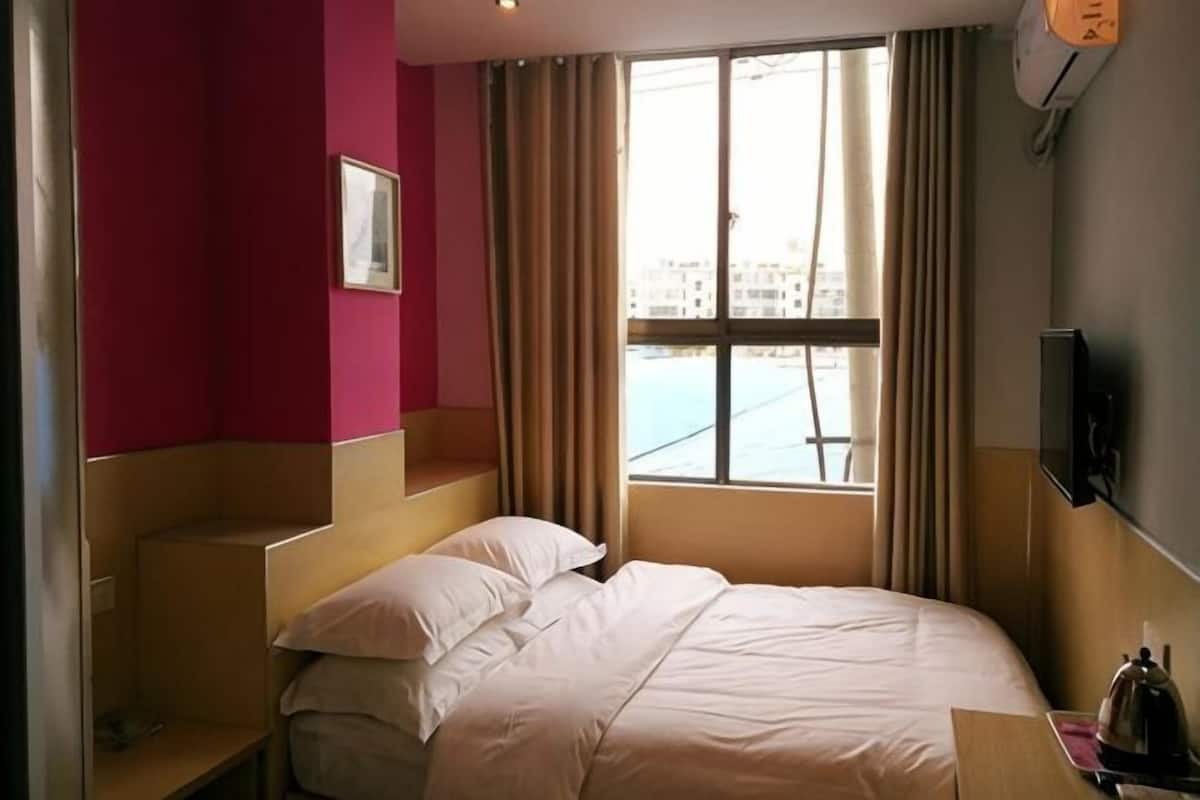 A hotel room with a bed, a TV, a window with curtains, and a view of buildings outside.