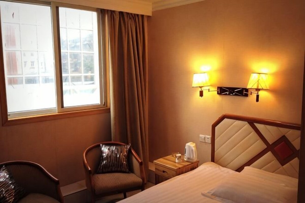 Una habitación de hotel con una cama, una silla, una mesita de noche y una ventana con cortinas.