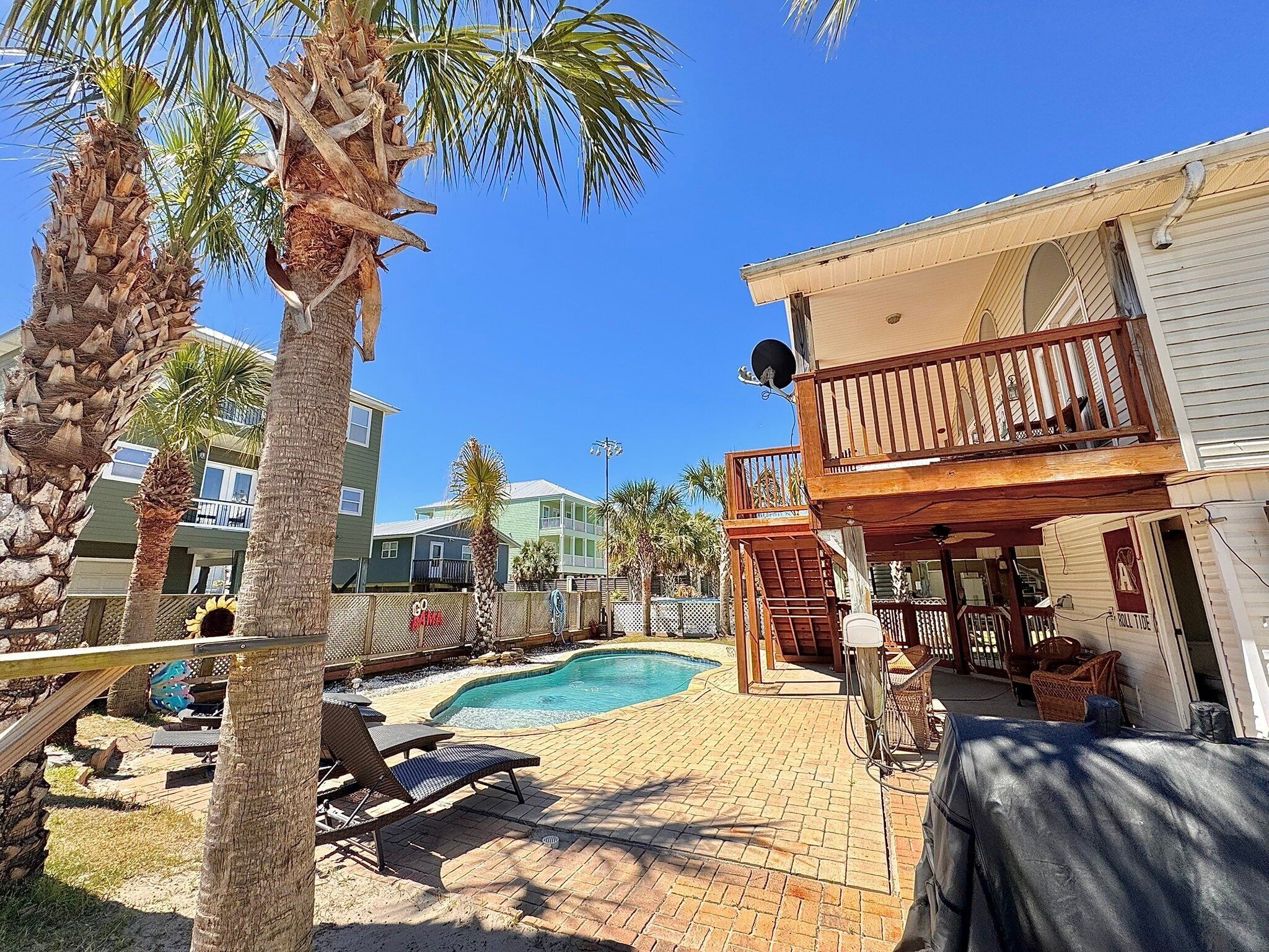 Un jardin avec une piscine, des palmiers et un patio couvert aménagé avec du mobilier d’extérieur.