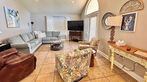 A living room with a sofa, armchairs, a coffee table, a TV, and a decorative mirror.