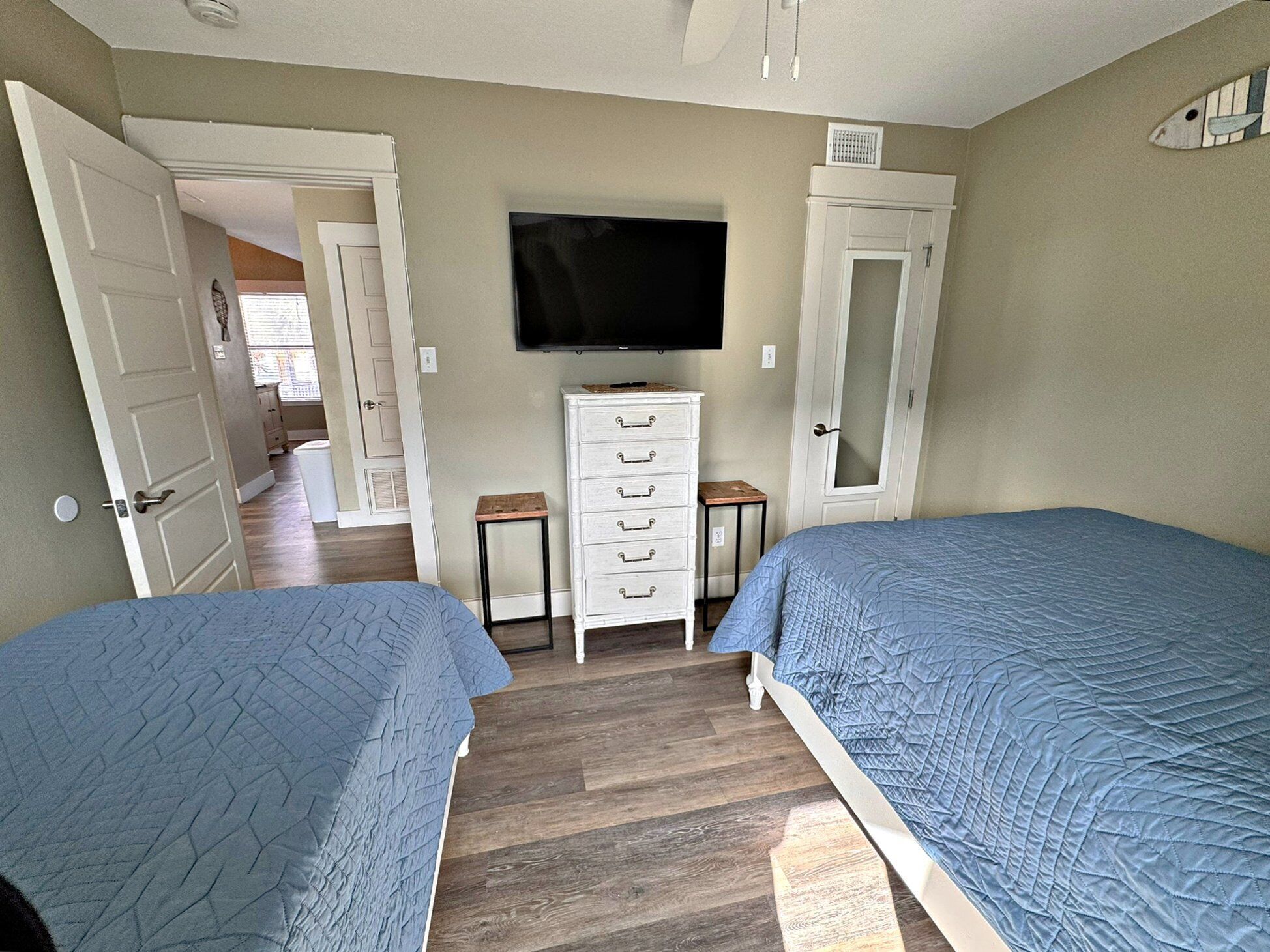 A bedroom with two beds, a dresser, a television, and a door leading to another room.