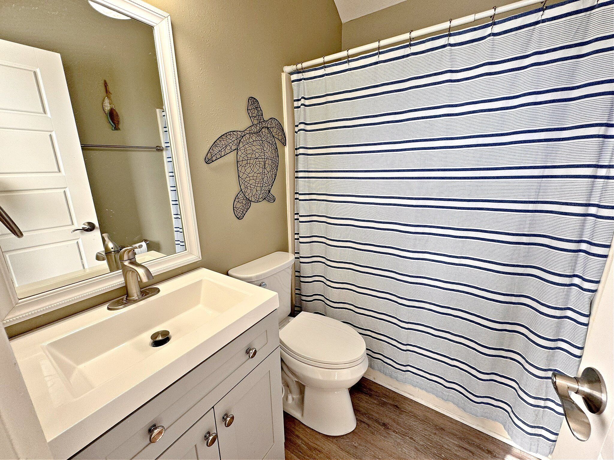 A bathroom with a striped shower curtain, a white toilet, a sink with a mirror, and a decorative turtle wall art.