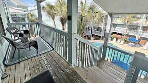 A wooden deck with outdoor furniture, a pool, and a view of a building with balconies. - Ocean Reef 504 (Gulf Shores)