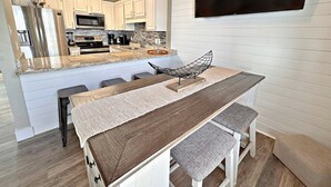 A modern kitchen with white cabinets, stainless steel appliances, a wooden island with bar stools, and a flat-screen TV mounted on the wall. - Ocean Reef 504 (Gulf Shores)