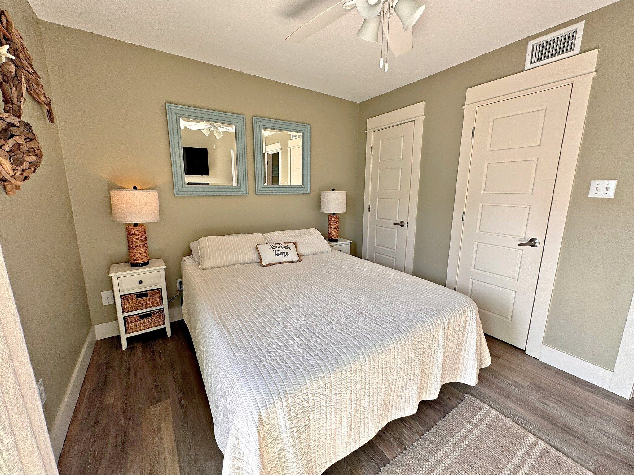 A bedroom with a bed, two nightstands, a ceiling fan, and two doors.