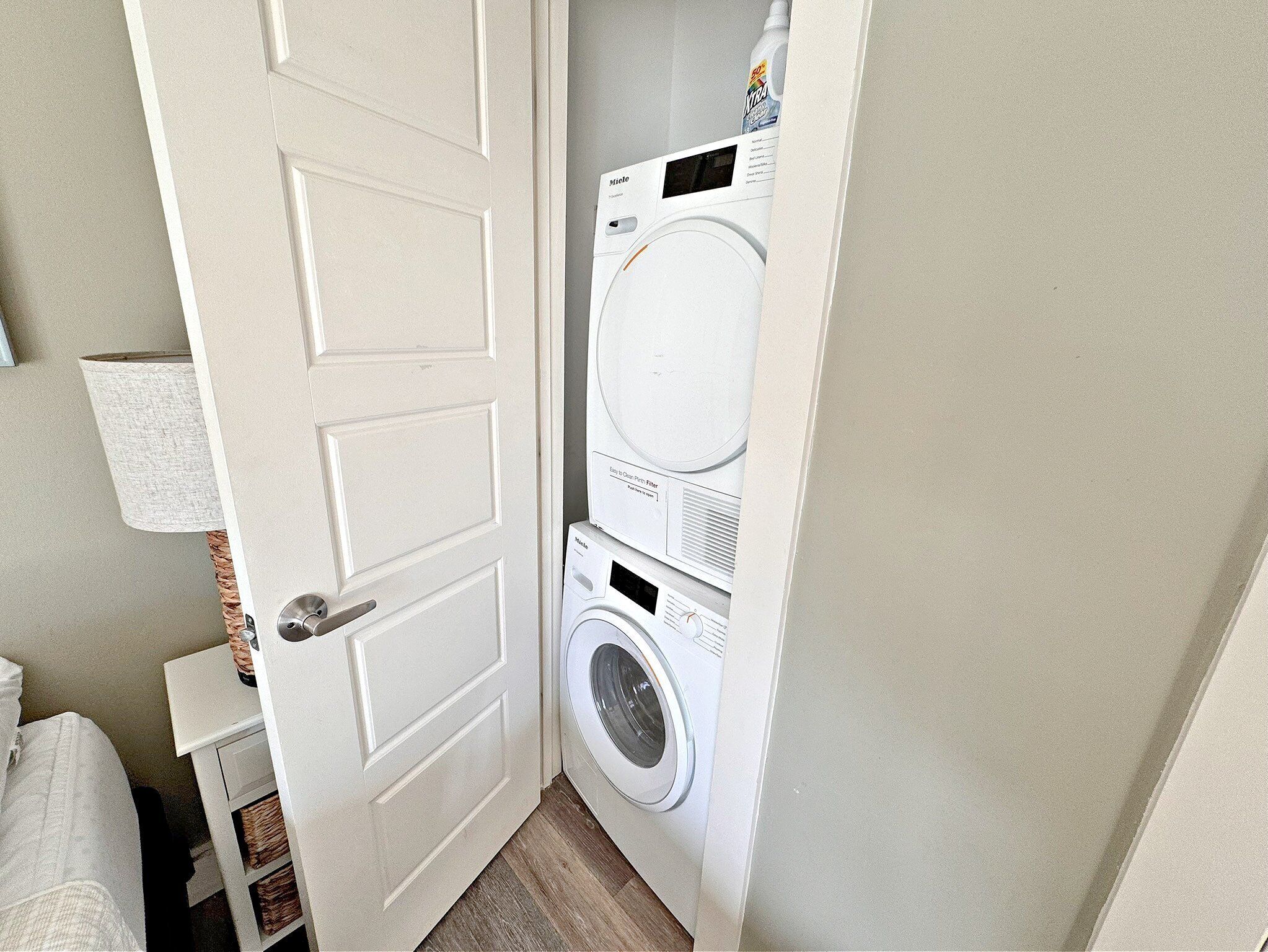 A laundry room with a stacked washer and dryer, a door, and a lamp.