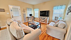 A living room with beige sofas, a TV, and a wooden coffee table. - The Rookery 202 (Gulf Shores)