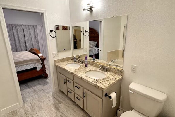 A bathroom with two sinks, a toilet, and a bed in the adjacent room. - Entire Home near Stadium (Glendale)