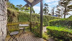 Une terrasse en bois avec une table et des chaises, entourée d’une clôture en bois et d’une végétation luxuriante.