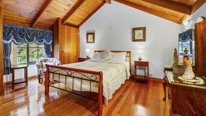 A spacious bedroom with a wooden ceiling, a large bed, a nightstand, a dresser, and a window with curtains. - StayAU Luxury Candlewick Cottage in Dandenong (Mount Dandenong)