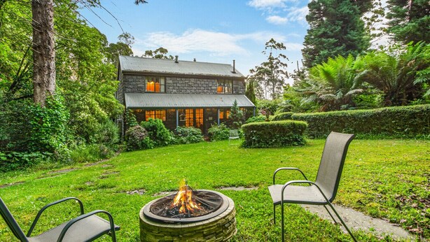 A stone house with a fire pit and two chairs in the yard. - StayAU Luxury Candlewick Cottage in Dandenong (Mount Dandenong)
