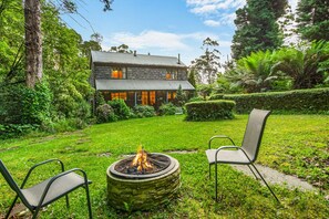 Une maison en pierre avec un foyer et deux chaises dans la cour.