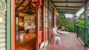A covered porch with a wooden floor, a white table and chairs, and a bed with a canopy in the background.