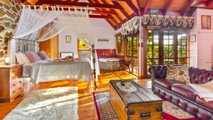 A spacious room with a large bed, a sitting area with a sofa, a wooden chest, and a stone wall. - StayAU Owls Croft Picturesque Cottage Valley View (Mount Dandenong)