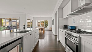A modern kitchen with white cabinetry, a stainless steel stove, and a large island with a sink.