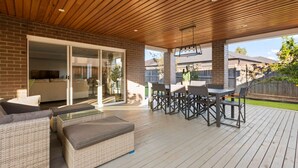 A covered patio with a wooden deck, outdoor furniture, and a glass door leading to an interior space.