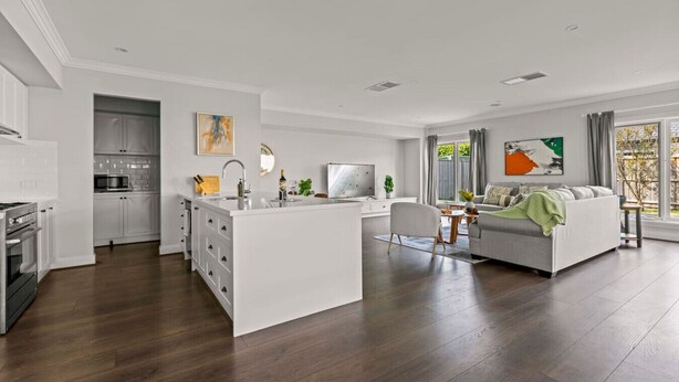 A modern kitchen with white cabinetry, a central island with a sink, and a dining area with a gray sofa and a small table.