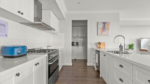 A modern kitchen with white cabinetry, a blue toaster, stainless steel appliances, and a wooden floor.