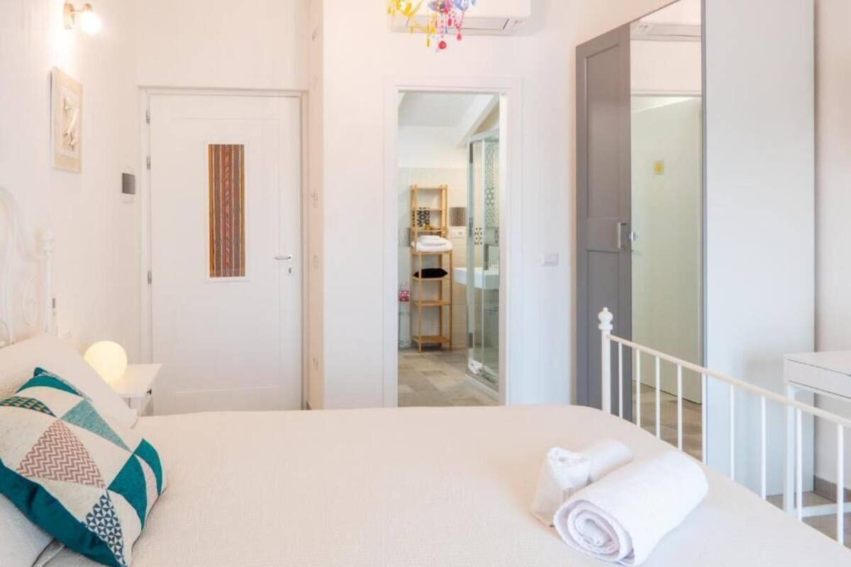 A hotel room with a bed, a bedside table, a white door, and a view into the bathroom.