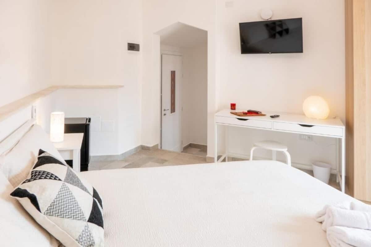 A hotel room with a bed, a desk, a chair, a TV, and a lamp.