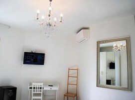 Une pièce avec un bureau blanc, une chaise en bois, un grand miroir et un lustre.
