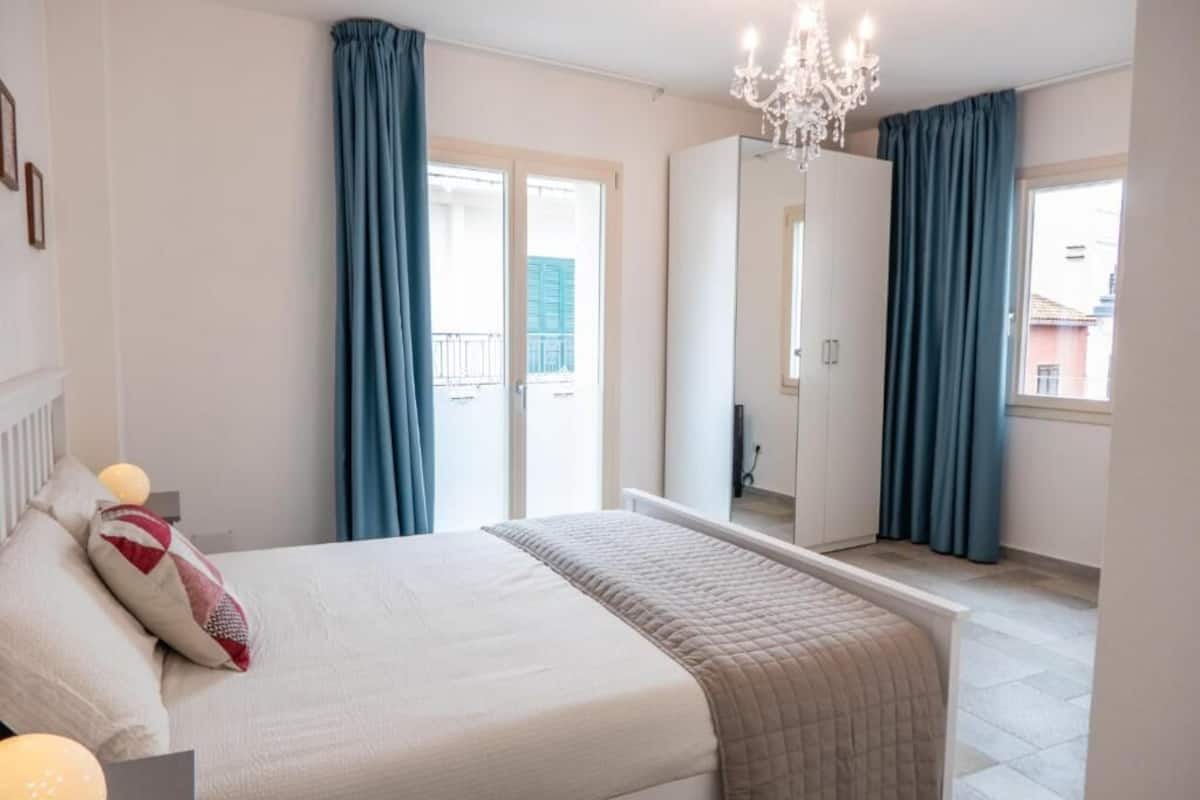 A bedroom with a bed, a large mirror, and a balcony with blue curtains.
