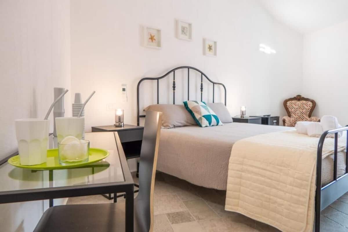 A neatly arranged bedroom with a bed, bedside tables, a chair, and a small table with cups and a glass.