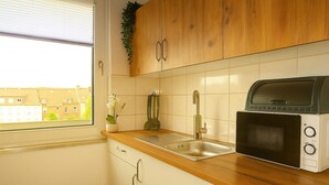 A kitchen with wooden cabinets, a stainless steel sink, a microwave, and a window with a view of buildings. - Livemore24 - Apartment 2 in Duisburg 24/7 check-in (Duisburg)