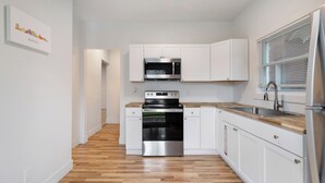A modern kitchen with white cabinets, a stainless steel oven, a microwave, and a wooden countertop.