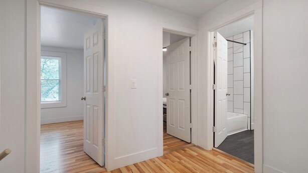 A hallway with wooden flooring, white walls, and open doors leading to different rooms.