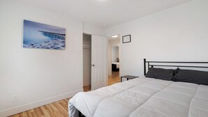 A bedroom with a bed, a white door, a small table, and a painting of a waterfall.