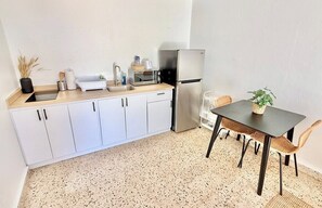 A compact kitchen with white cabinets, a stainless steel refrigerator, a sink, and a dining area with a table and chairs.