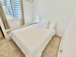 Une chambre à coucher avec un lit, une table de chevet, une lampe et une fenêtre avec des rideaux.