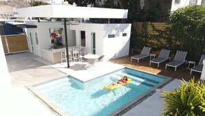 A swimming pool with a person on a float, lounge chairs, and a patio area with a table and chairs. - Villa Coco: Private Pool | 5 Min Walk to Beach (San Juan)