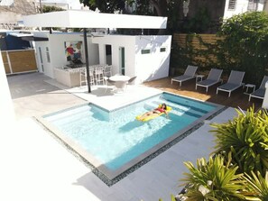 A swimming pool with a person on a float, lounge chairs, and a patio area with a table and chairs. - Villa Coco: Private Pool | 5 Min Walk to Beach (San Juan)