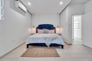 A modern bedroom with a large bed, bedside lamps, and a view into another room. - Villa Coco: Private Pool | 5 Min Walk to Beach (San Juan)