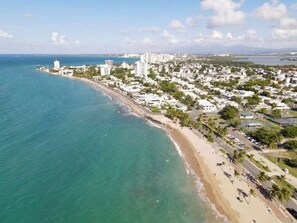 A coastal cityscape with a beach, buildings, and a clear sky. - Villa Coco: Private Pool | 5 Min Walk to Beach (San Juan)