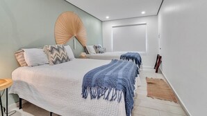 A modern bedroom with two beds, a large fan, and a window. - Villa Coco: Private Pool | 5 Min Walk to Beach (San Juan)