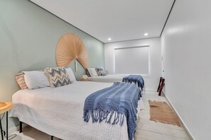 A modern bedroom with two beds, a large fan, and a window. - Villa Coco: Private Pool | 5 Min Walk to Beach (San Juan)