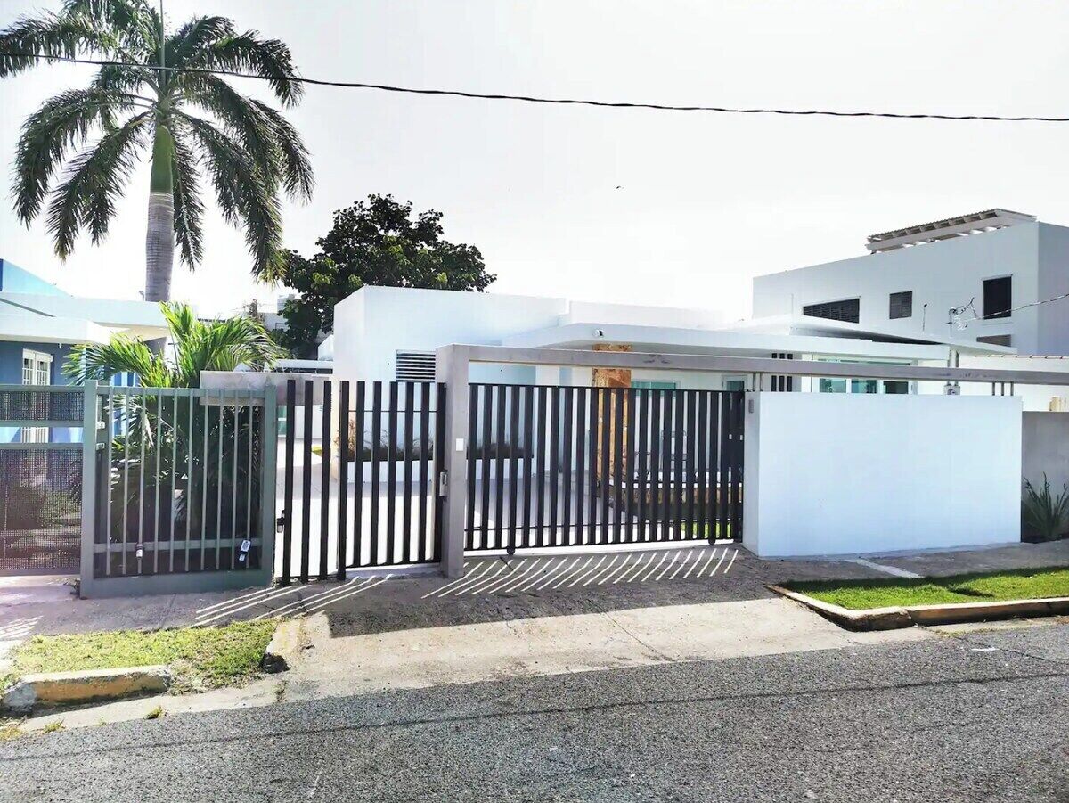 A gated entrance to a modern building with a white facade and a palm tree in the background.